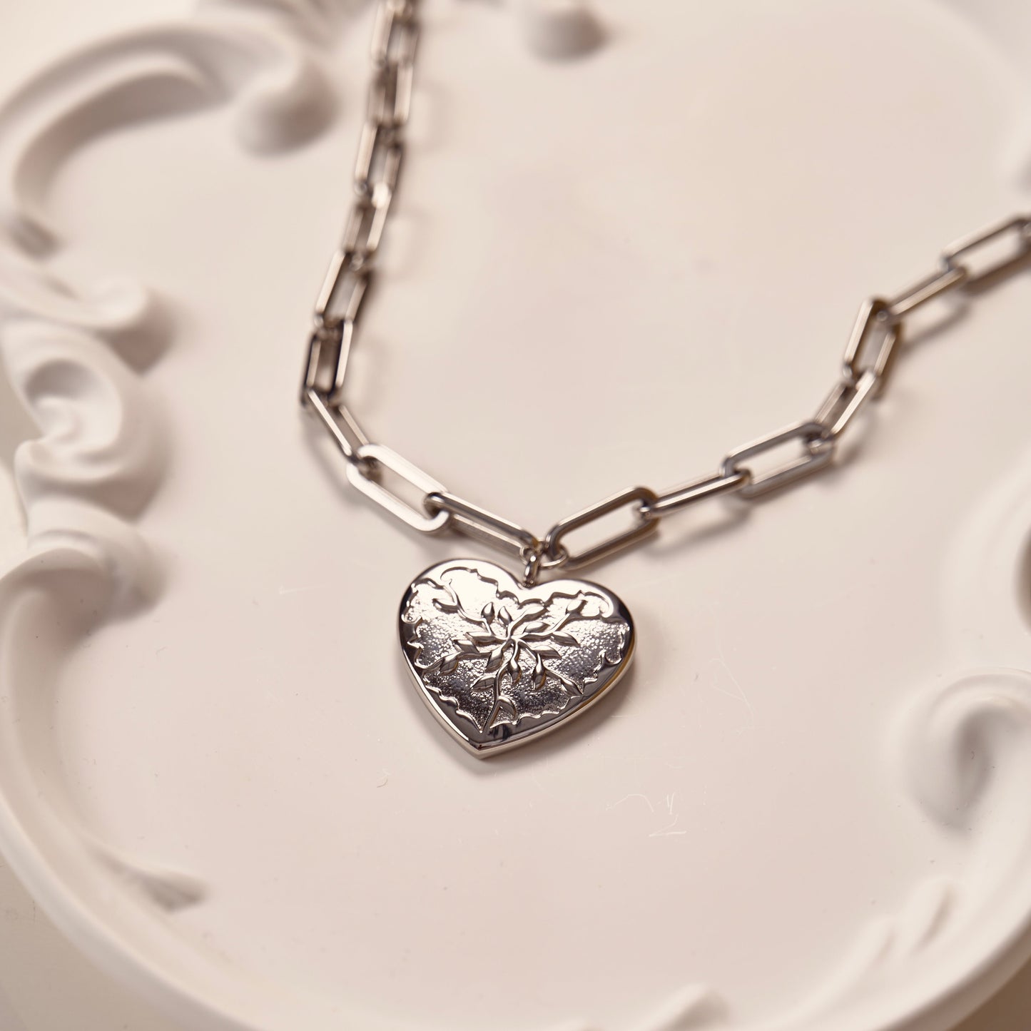 Collier argenté en acier inoxydable, avec pendentif en forme de cœur, avec un design unique rappelant des feuilles d'olivier. Chaîne à grosse maille réglable. Bijou résistant, élégant et symbolique.