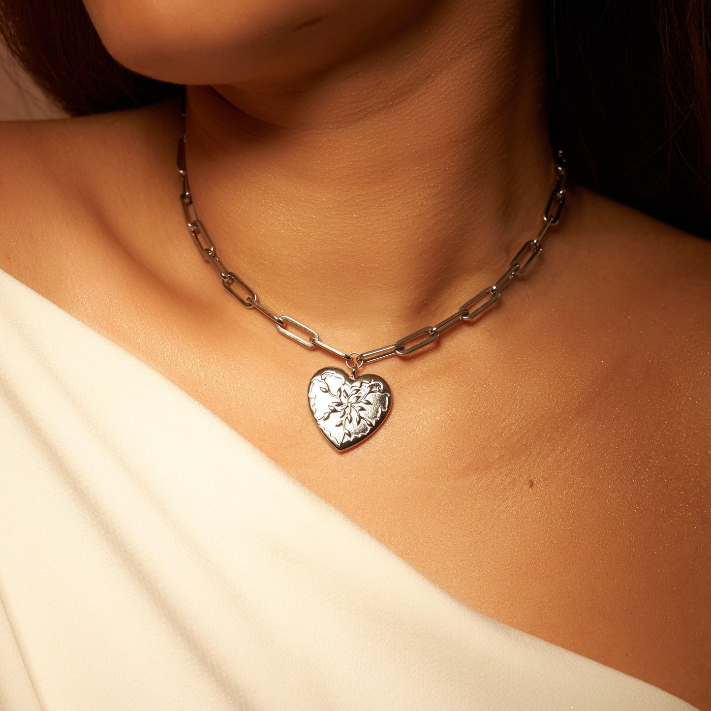 Collier argenté en acier inoxydable, avec pendentif en forme de cœur, avec un design unique rappelant des feuilles d'olivier. Chaîne à grosse maille réglable. Bijou résistant, élégant et symbolique.